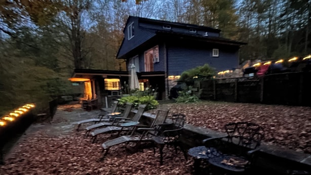 Un chalet rustique doté d’un foyer et de sièges d’extérieur, entouré d’un sol recouvert de feuilles.