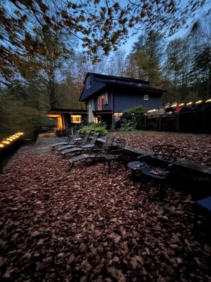 A rustic cabin with a fire pit and outdoor seating, surrounded by a leaf-covered ground. - Private Lakefront Cottage, Panoramic Lake Views. 
Fish, Row, Kayak, Pet-Friendly (Jeffersonville)