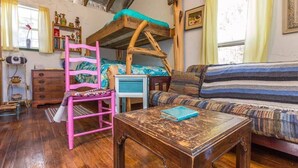 Een rustieke kamer met een stapelbed, een roze stoel, een gestreepte bank en een houten tafel.