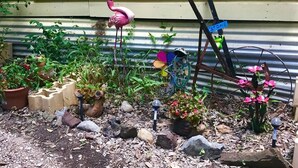 Een tuin met diverse planten, een flamingo decoratie, en een bord met een welkomstboodschap.