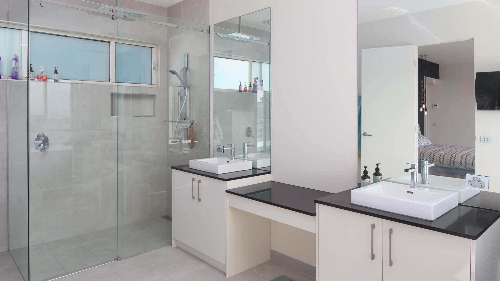 A modern bathroom with a glass shower enclosure, two sinks, and a large mirror.