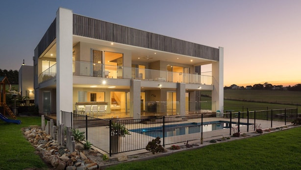 Une maison moderne à deux étages, dotée d’une piscine, de grandes fenêtres et d’une cour clôturée.