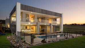 A modern two-story house with a swimming pool, large windows, and a fenced yard.