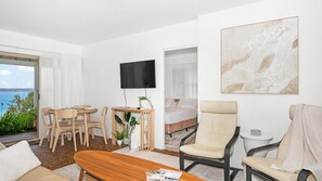 Une chambre d’hôtel comprenant un coin repas, un lit, une télévision et une grande fenêtre donnant sur la mer.