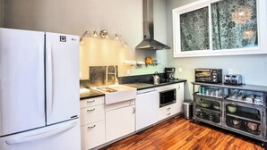 Uma cozinha moderna com geladeira branca, coifa de aço inoxidável e uma janela com cortinas florais.