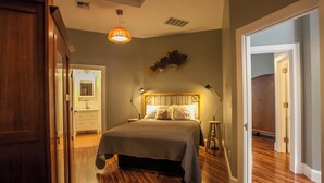 Quarto com piso de madeira, cama com cabeceira, luminárias laterais e um lustre.