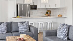 A modern kitchen with stainless steel appliances, white cabinetry, and a grey sofa set.