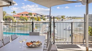 A balcony with a table set for dining, overlooking a marina with boats and houses in the background.