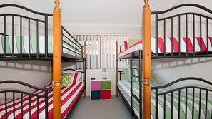 A dormitory room with bunk beds, a small desk, and storage drawers.