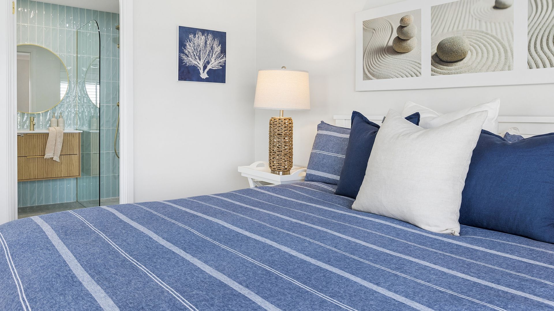 Un dormitorio con cama, mesita de noche, lámpara y una obra de arte en la pared.