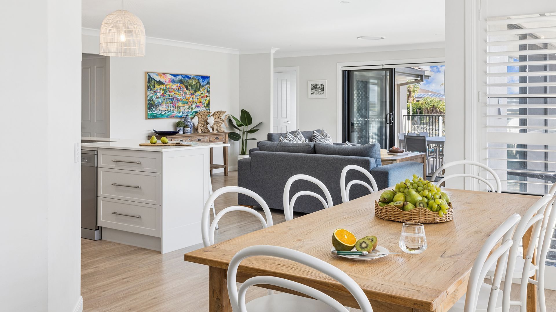 A modern kitchen with white cabinets, a dining table with white chairs, and a balcony with a view.