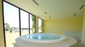 A hot tub in a room with large windows and a view of a pool area. - Parque Botanico Holiday Rentals (Estepona)