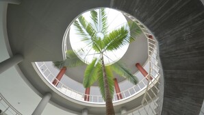 A circular atrium with a central palm tree, a glass railing, and a modern architectural design. - Parque Botanico Holiday Rentals (Estepona)