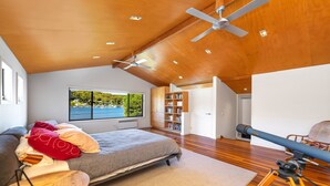 Une chambre à coucher comprenant un lit, un ventilateur de plafond, une grande fenêtre donnant sur un port et une bibliothèque.