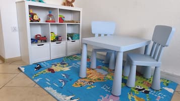 A child's playroom with a white bookshelf, a blue and white chair, and a world map rug.