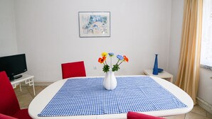 Une pièce avec une nappe à carreaux, un vase rempli de fleurs, un tableau encadré accroché au mur et un téléviseur posé sur une petite table.