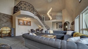 Ein geräumiges Wohnzimmer mit einem großen, grauen Ecksofa, einem Couchtisch und einer Treppe mit schmiedeeisernem Geländer.