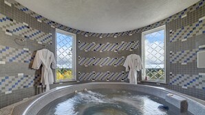 Ein Wellnessbereich mit Whirlpool, gefliesten Wänden und zwei Fenstern mit Aussicht.
