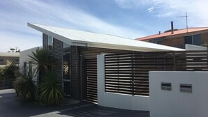 Una casa moderna con techo inclinado, cerca de madera y un pequeño jardín con palmeras.
