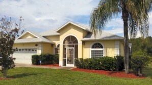 A two-story house with a garage, a front entrance with a glass door, and a small front yard with red mulch and a palm tree. - Stunning Lakeview Villa (Davenport)