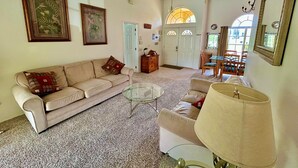 A spacious living room with a beige sofa, a glass coffee table, and a dining area with wooden chairs. - Stunning Lakeview Villa (Davenport)