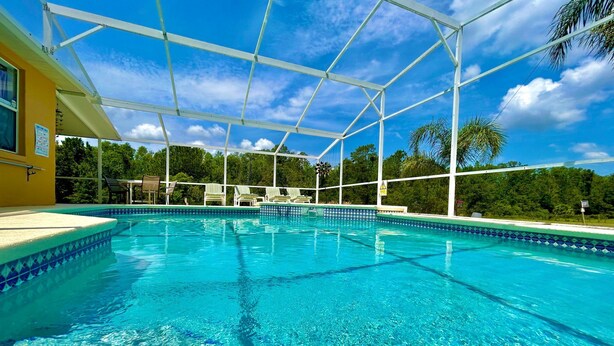 A clear blue pool with a white deck and lounge chairs, surrounded by a covered area with a view of trees. - Stunning Lakeview Villa (Davenport)