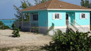 Una casa de dues plantes de color turquesa amb un porxo, una petita escala i vista a l'oceà.
