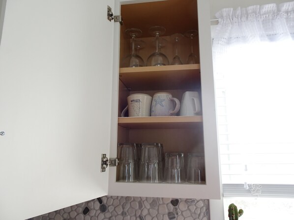 A kitchen cabinet with shelves holding glassware, mugs, and pitchers.