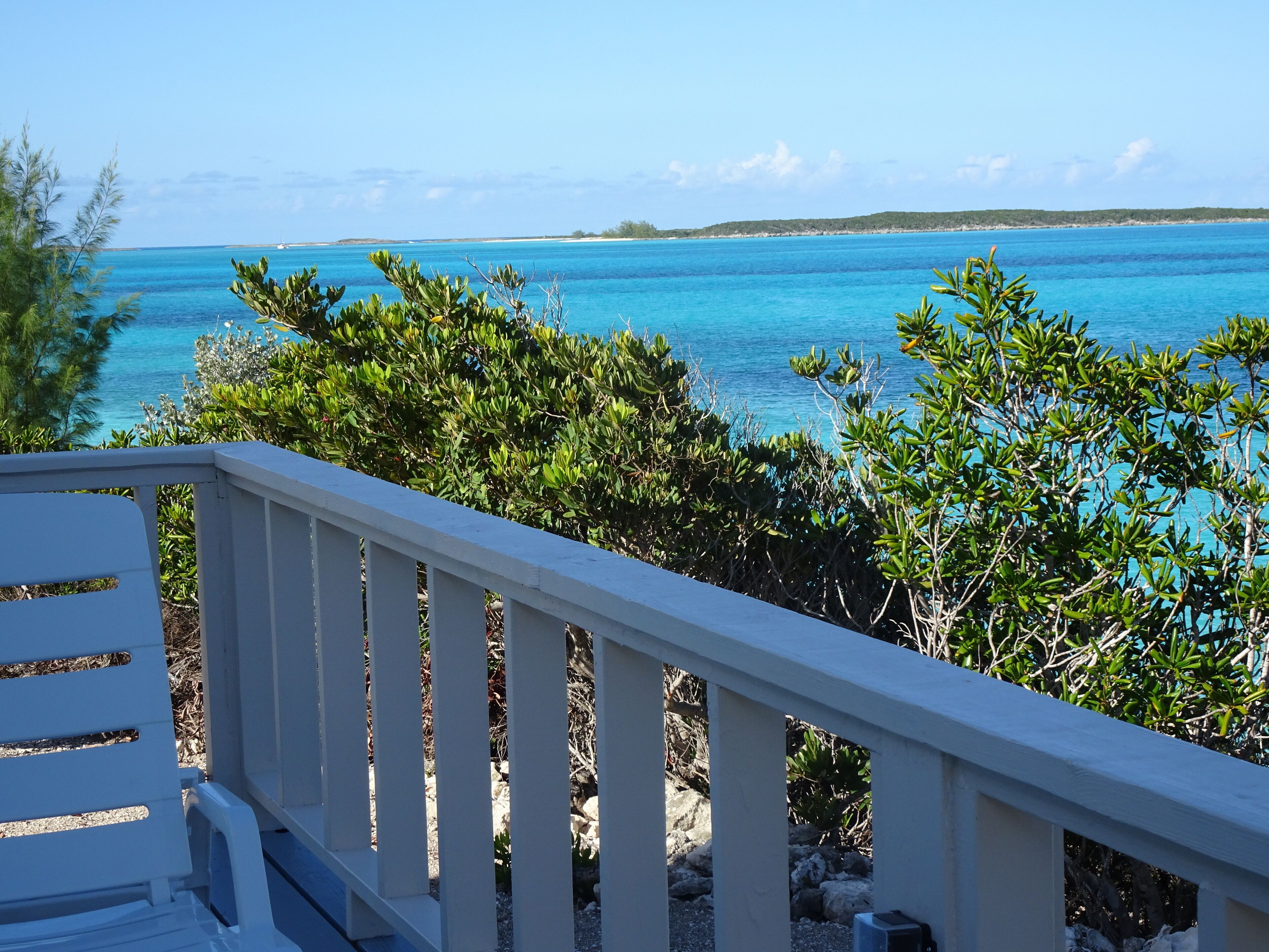 Un balcon blanc offrant une vue sur des eaux turquoise et une terre lointaine.