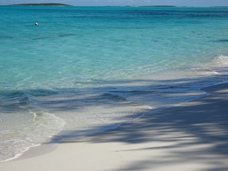 A beach with clear turquoise water, gentle waves, and a sandy shore.