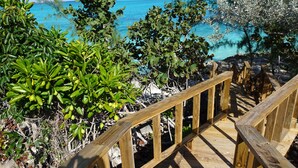 Unes escales de fusta que condueixen a una platja amb aigua turquesa i vegetació exuberant.