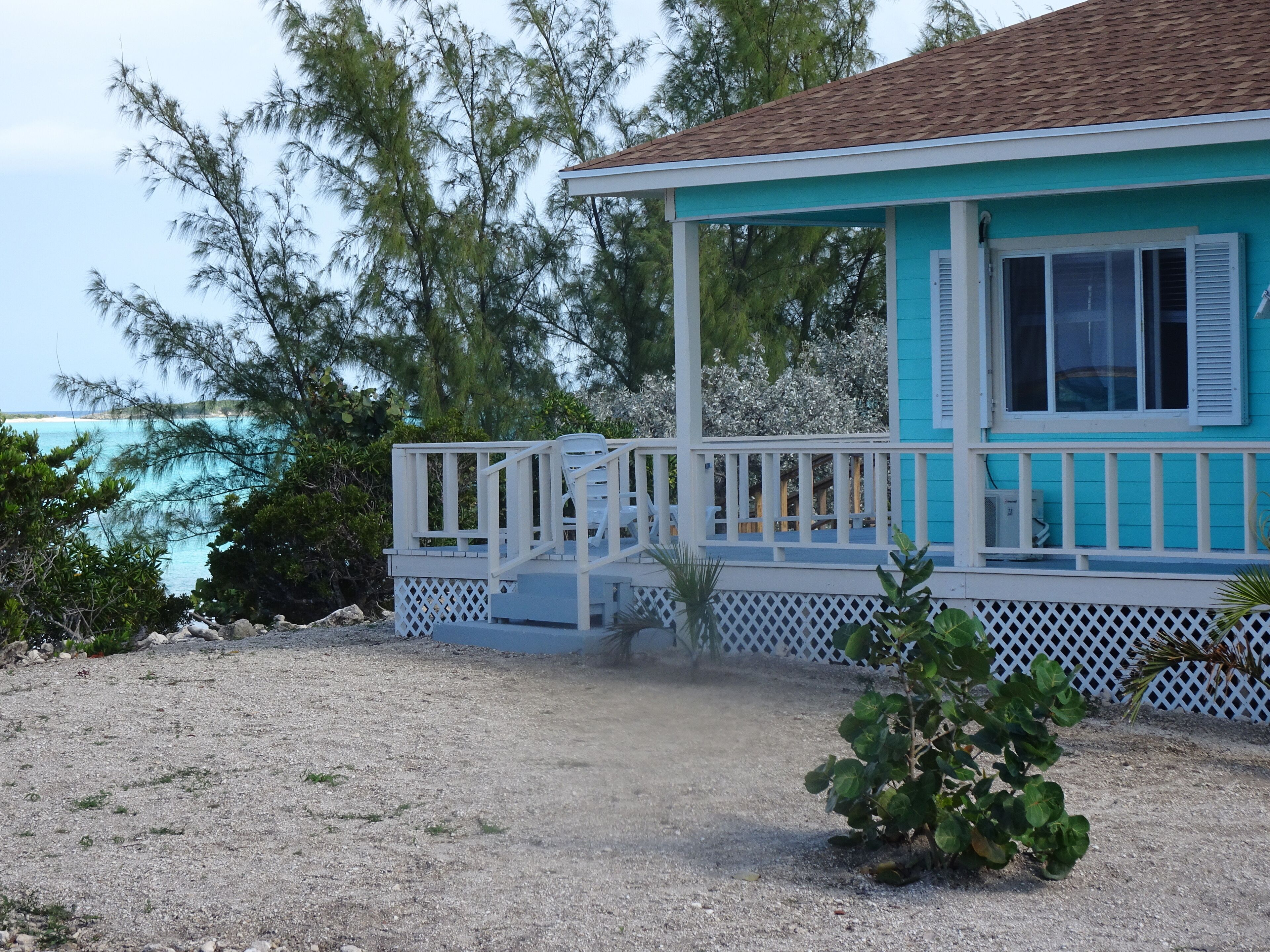 A turquoise building with a white porch and a small garden area.