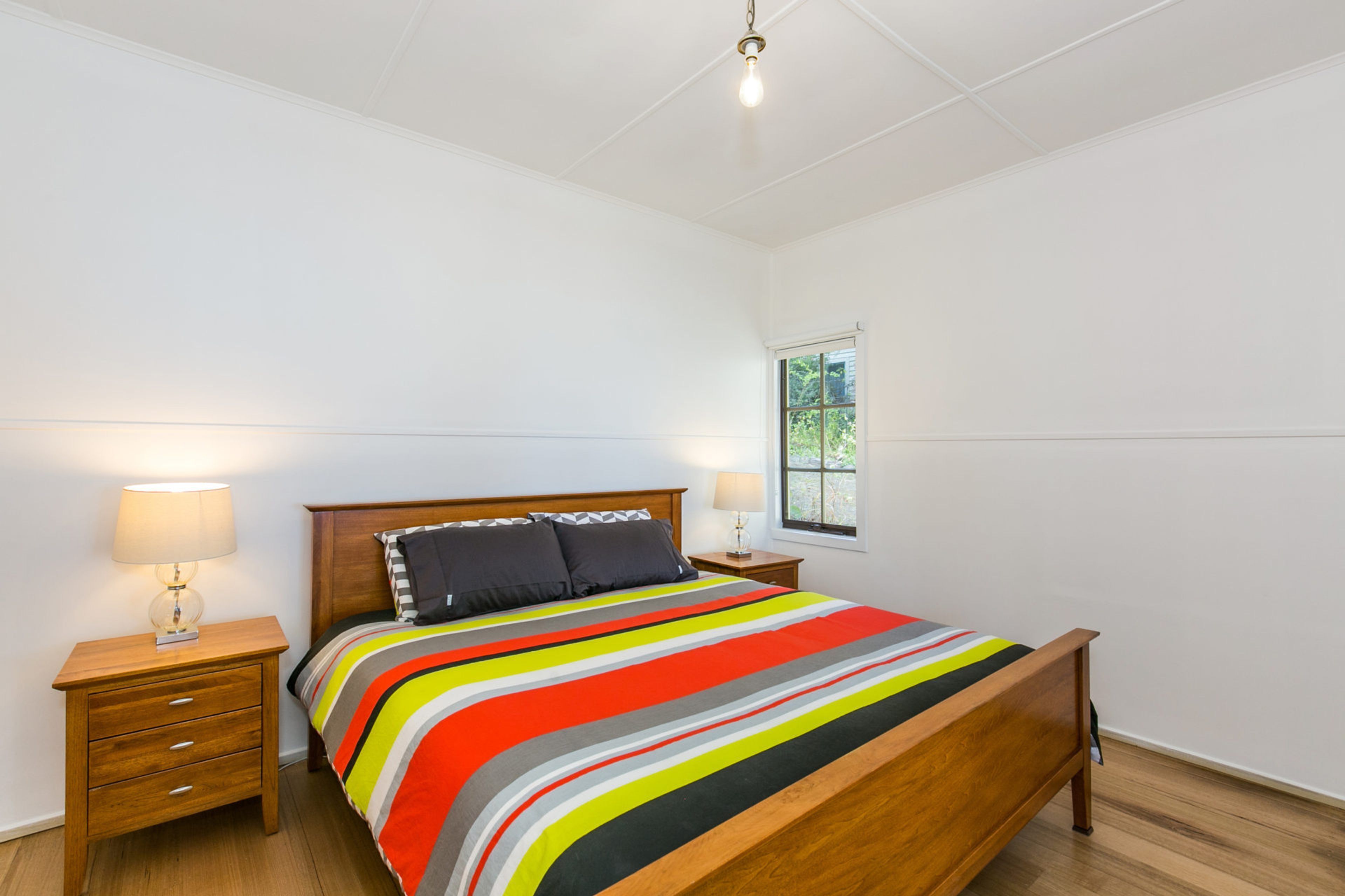 Een slaapkamer met een houten bed, een nachtkastje, een lamp en een raam.