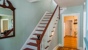 Una escalera de madera con barandillas blancas que conduce a un cuarto con piso de madera y una puerta al fondo.