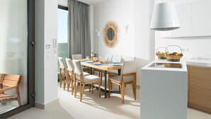 A modern dining area with a wooden table and chairs, a white pendant light, and a kitchen counter with baskets.