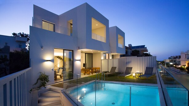 A modern two-story house with a swimming pool, outdoor seating, and a well-lit entrance.
