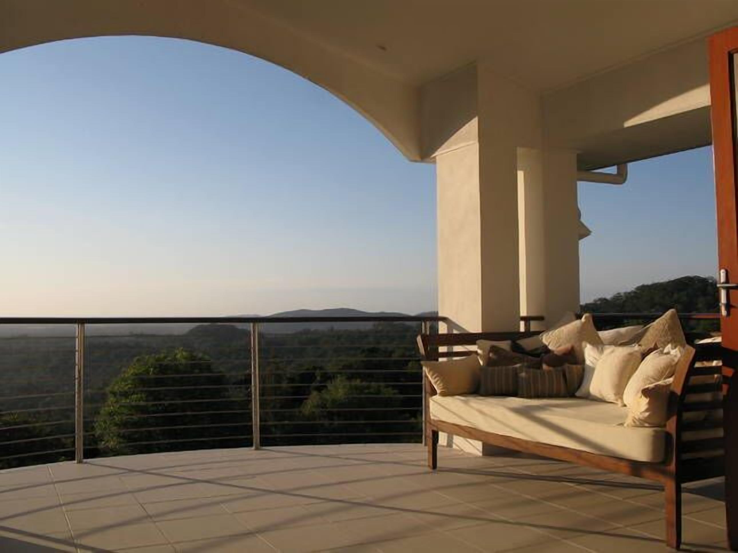 A balcony with a sofa and cushions, offering a view of a hilly landscape.