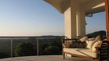A balcony with a sofa and cushions, offering a view of a hilly landscape.