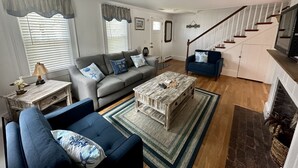 A living room with a grey sofa, blue armchair, and coffee table, a staircase, and a fireplace. - SHORT WALK TO BEACH Central A/C (Dennis Port)