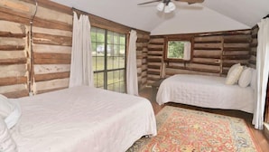 A log cabin room with two beds, a ceiling fan, and a large window.