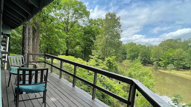A wooden deck with a railing overlooking a river and dense greenery.