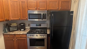 A kitchen with wooden cabinets, a stainless steel refrigerator, a microwave, a stove, and a sink.