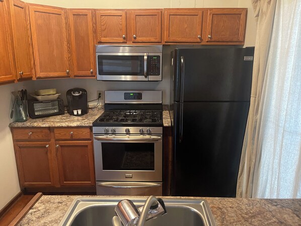 A kitchen with wooden cabinets, a stainless steel refrigerator, a microwave, a stove, and a sink.