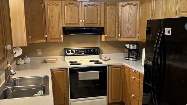 A kitchen with wooden cabinets, a stainless steel sink, a black refrigerator, and a gas stove.