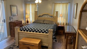 A bedroom with a wooden bed, bedside tables, a nightstand, a ceiling fan, and a window with curtains.