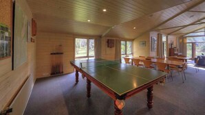 Una mesa de ping pong en una habitación con paredes de madera y ventanas grandes.