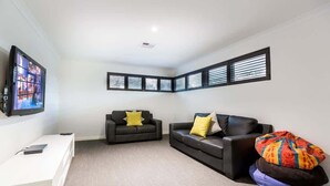 A modern living room with a flat-screen TV, two black sofas with yellow and patterned cushions, a white console table, and a large window with blinds. - Lilywood—Minutes from Wineries & Yallingup Beach (Yallingup)
