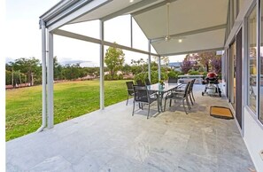 Uma área de varanda coberta com mesa, cadeiras, churrasqueira e vista para a paisagem ao redor.