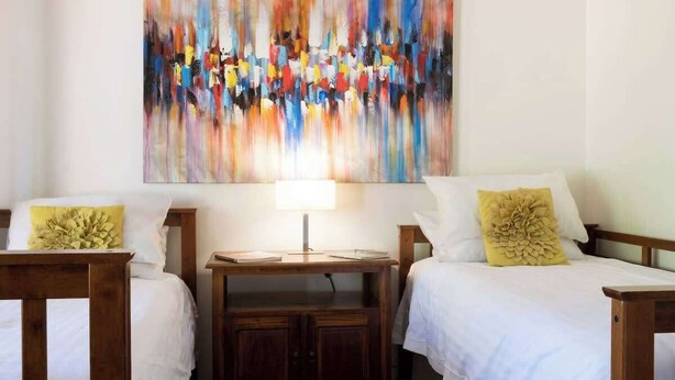Een hotelkamer met twee bedden, een nachtkastje, een lamp en een kleurrijk abstract schilderij aan de muur.