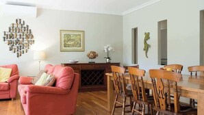 Een woonkamer met een bank, een eettafel met stoelen, een open haard en een wandlamp.